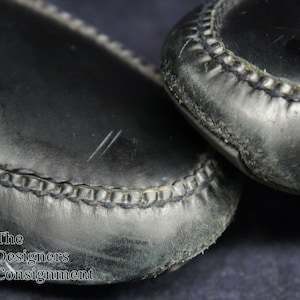 May include: Close-up of the black leather soles of a pair of shoes. The shoes have a stitched seam around the edge of the sole.