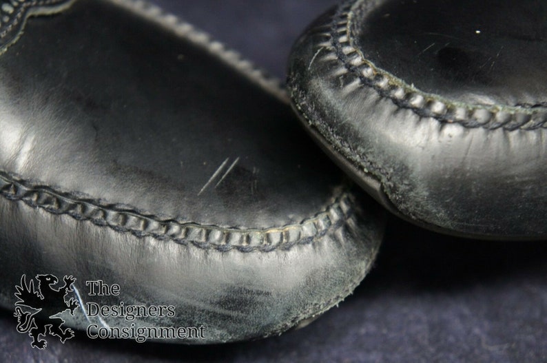 May include: Close-up of the black leather soles of a pair of shoes. The shoes have a stitched seam around the edge of the sole.