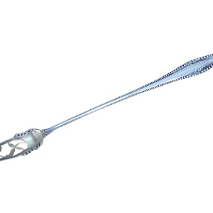 May include: A silver-colored serving fork with an ornate handle and a long, slender body. The fork features a decorative pattern along the edges and a detailed design at the handle's end. The tines are pointed and the fork is designed for serving.