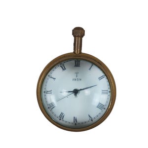 May include: A brass pocket watch with a white face and black Roman numeral hour markers. The watch has a magnifying glass over the face and the text "1939" on the face.