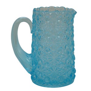 May include: A light blue glass pitcher with a textured, starburst pattern. The pitcher has a curved handle and a scalloped rim. The pitcher is made of glass and is suitable for serving beverages.