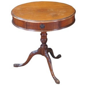 May include: A round wooden table with a single drawer and three legs. The table is made of dark wood and has a simple, elegant design.
