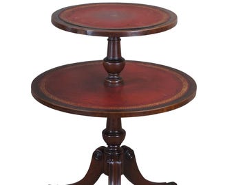 May include: A two-tiered mahogany side table with a red leather top. The table has a turned pedestal base and three cabriole legs.