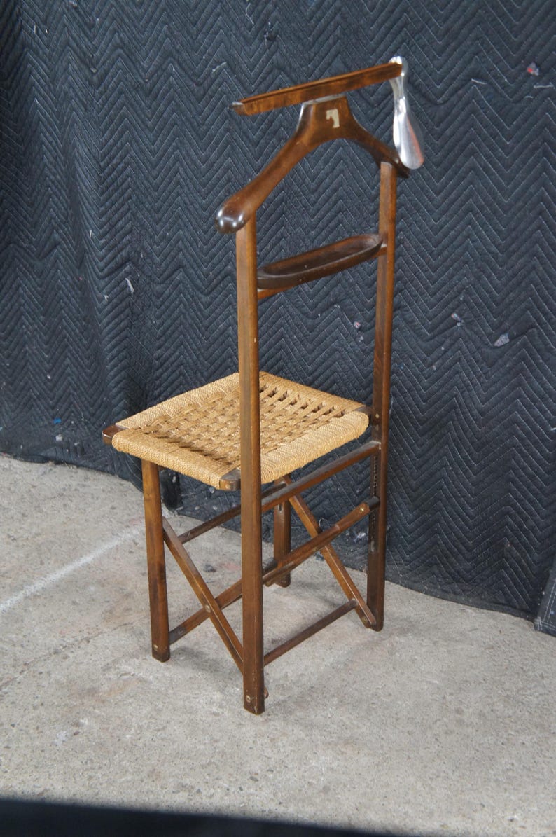 May include: A vintage wooden valet chair with a woven seat and a built-in coat hanger. The chair has a dark brown finish and a small shelf. The coat hanger has a number 1 on it. The chair is designed to hold clothing.