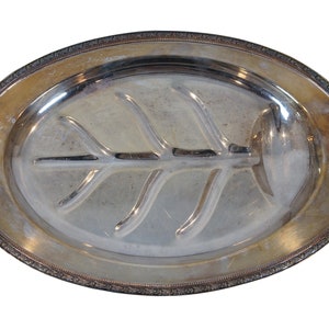 May include: A silver oval serving platter with a leaf-shaped design in the center. The platter has a decorative border.
