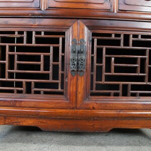 Pode incluir: Close-up de um arm&aacute;rio de madeira com acabamento castanho-avermelhado escuro. O arm&aacute;rio apresenta intrincados trabalhos de treli&ccedil;a geom&eacute;trica nas portas e gavetas, com ferragens de metal escuro. O design sugere um estilo antigo ou de inspira&ccedil;&atilde;o asi&aacute;tica.