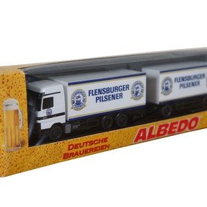 May include: A white toy truck with two trailers, both labeled "Flensburger Pilsener" and "Deutsche Brauereien". The truck is in a yellow and orange box with the word "ALBEDO" printed on it.