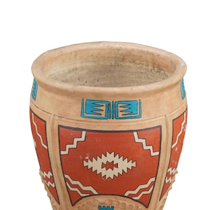 May include: A beige ceramic planter with a Southwestern design. The planter features a red and white geometric pattern, with blue accents. The rim and base have a textured, decorative edge. The planter is empty.