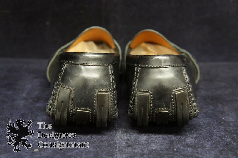 May include: A pair of black leather loafers with a textured design on the back. The loafers have a brown leather lining and a rubber sole.