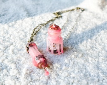May include: A pink glass bottle and a pink glass vial on a silver chain necklace. The bottle and vial are filled with a pink liquid and have a dripping effect.