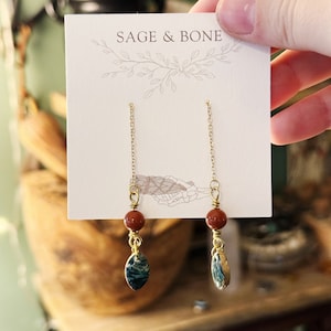 May include: Gold chain earrings with a red bead and a blue and green stone pendant. The earrings are displayed on a white card with the text "Sage & Bone".