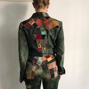 Op de afbeelding: Groene suède jas en broek set met patchwork details. De jas heeft een patchwork ontwerp op de rug en schouders. De broek heeft patchwork zakken. Een unieke, vintage-geïnspireerde outfit.