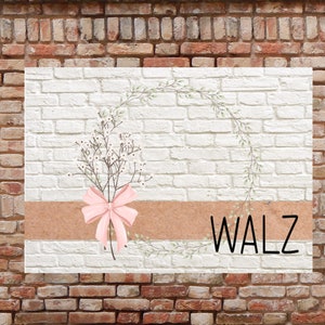 May include: A white brick wall with a wreath of green leaves and a pink bow. The text "WALZ" is written in black letters on a brown background.