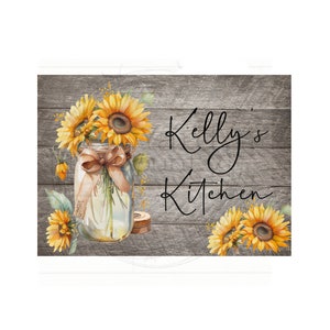 May include: A rustic wooden sign with the text "Kelly's Kitchen" in black script. A mason jar filled with sunflowers and a brown ribbon sits on the left side of the sign.
