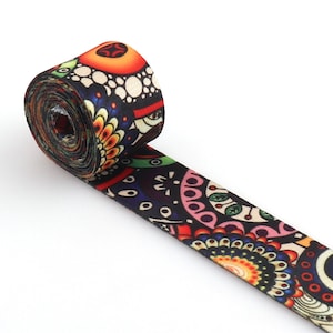 Peut inclure: Un ruban à motifs colorés avec un fond noir et des couleurs vives comme le rouge, l'orange, le jaune, le vert, le bleu et le rose. Le ruban est enroulé et le motif est visible sur le rouleau.