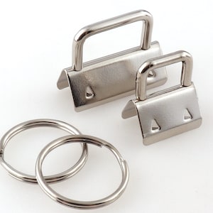 Puede incluir: Dos llaveros de metal plateado en forma de D con un bucle a cada lado. Los llaveros están unidos a dos anillos de llaves de metal plateado.