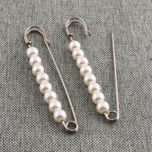 以下が含まれることがあります： 白い真珠のビーズが付いた銀色の安全ピンが2本。ピンが開いていて、使用できます。