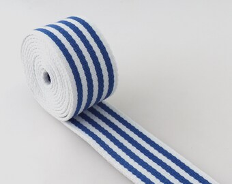 May include: A roll of white and blue striped webbing. The webbing is tightly wound into a roll, with the end of the webbing extending out. The stripes are a vibrant blue color and run parallel to each other.