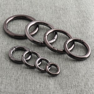 May include: A set of six black metal key rings of varying sizes. The rings are all closed and have a smooth, polished finish.