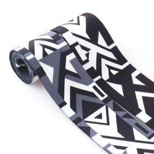 May include: Black and white patterned fabric ribbon with a geometric design. The ribbon is rolled up and the pattern is visible on both sides.