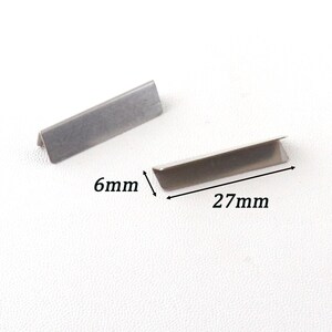 May include: Two silver metal corner protectors, each measuring 27 mm long and 6 mm wide.