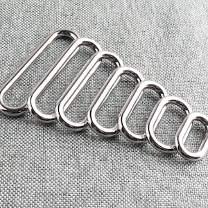 May include: A set of seven silver metal oval rings of varying sizes. The rings are arranged in a graduated size order, with the largest ring at the top and the smallest ring at the bottom.