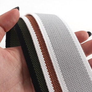 May include: Three different types of woven webbing, one with white and brown stripes, one with white and orange stripes, and one with black and green stripes.