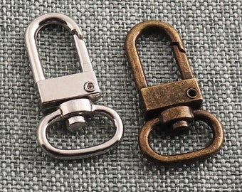 Puede incluir: Dos cierres metálicos, uno plateado y otro de latón antiguo, con un anillo en D en cada uno. Los cierres se utilizan para sujetar artículos a bolsos, llaveros u otros accesorios.