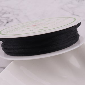 Op de afbeelding: Een spoel met zwart koord gewikkeld rond een witte kunststof spoel met een label in Chinese karakters.