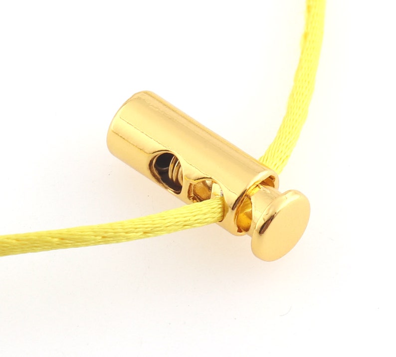 May include: Gold-toned cord lock with a spring mechanism. The cord lock is threaded onto a yellow cord.
