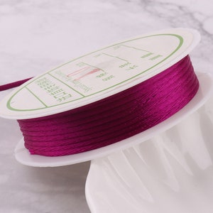 May include: A spool of deep purple thread wound around a white plastic bobbin. The bobbin has a label with text in a foreign language.