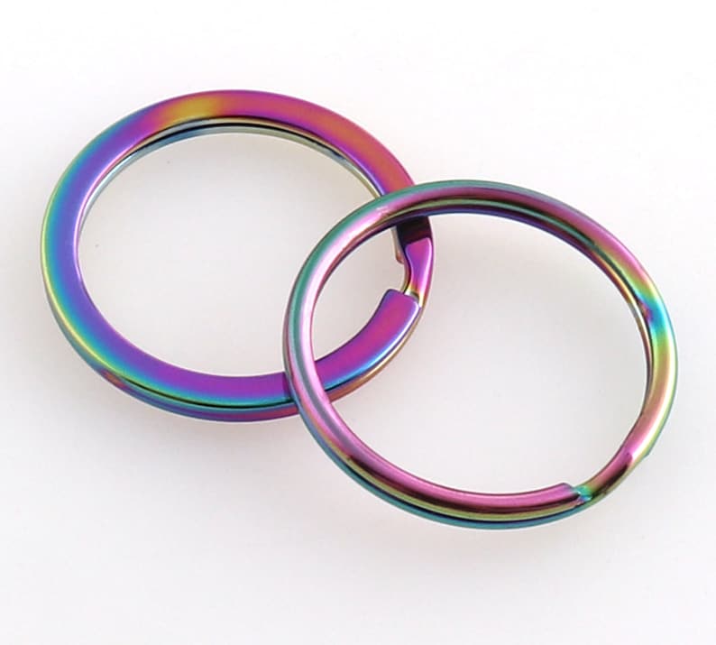 May include: Two iridescent key rings, one slightly larger than the other, are linked together. The rings are a rainbow of colors, including purple, blue, green, yellow, and orange.