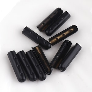 May include: A group of ten black metal cord ends with a small hole in the center of each end. The cord ends are scattered on a white surface.
