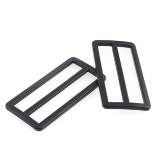 May include: Two black metal slider buckles. The buckles are rectangular with two parallel bars across the center.