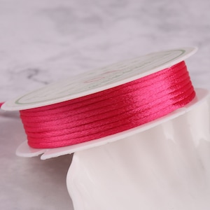 May include: A spool of bright pink satin cord. The cord is wound around a white plastic spool.
