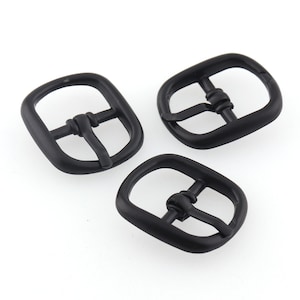 May include: Three black metal belt buckles. Each buckle has a rectangular shape with rounded corners and a center bar with a small loop.