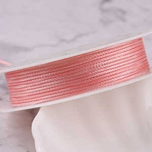 Peut inclure: Une bobine de cordon ciré rose, enroulée sur une bobine en plastique blanche.