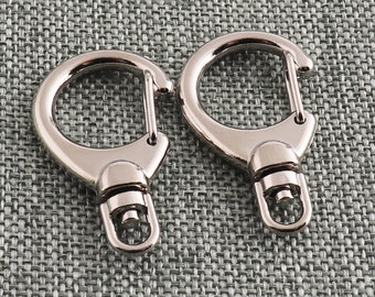 May include: Two silver metal key rings with a swivel clasp. The key rings are on a gray textured background.