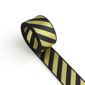 May include: Black and gold striped ribbon with a diagonal pattern. The ribbon is rolled up and the end is hanging down.