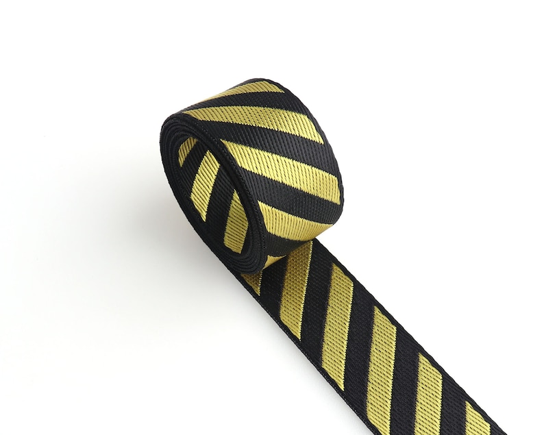 May include: Black and gold striped ribbon with a diagonal pattern. The ribbon is rolled up and the end is hanging down.