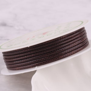 May include: A spool of brown waxed cord, wound around a white cardboard spool. The cord is smooth and has a subtle braided texture.