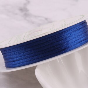May include: A spool of dark blue satin cord, wound around a white plastic spool. The cord is smooth and shiny.