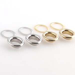 May include: Three sets of metal eyelets in silver and gold. Each set includes a larger oval-shaped eyelet and a smaller circular eyelet.