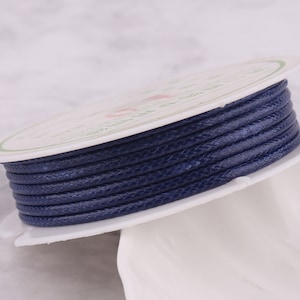 Peut inclure: Une bobine de cordon ciré bleu foncé. Le cordon est enroulé serré autour d'une bobine en plastique blanche avec une étiquette.