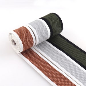 May include: Three rolls of white cotton webbing with colored stripes. The stripes are brown, gray, and black.