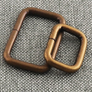 May include: Two antique gold-toned metal D-rings. The larger ring is approximately 5 cm wide and the smaller ring is approximately 2.5 cm wide.
