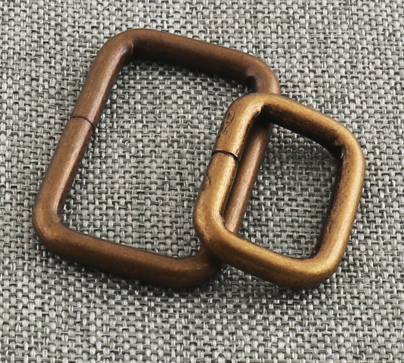 May include: Two antique gold-toned metal D-rings. The larger ring is approximately 5 cm wide and the smaller ring is approximately 2.5 cm wide.