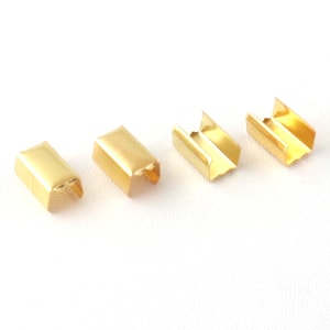 Puede incluir: Cuatro hebillas deslizantes de metal dorado, cada una con forma rectangular y una abertura en forma de U. Las hebillas est&aacute;n dispuestas en una fila sobre una superficie blanca.