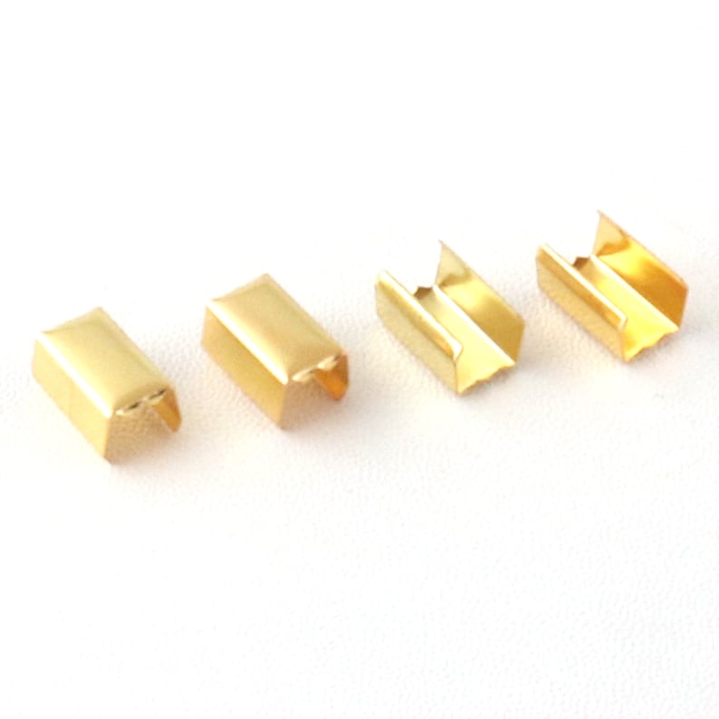 Puede incluir: Cuatro hebillas deslizantes de metal dorado, cada una con forma rectangular y una abertura en forma de U. Las hebillas est&aacute;n dispuestas en una fila sobre una superficie blanca.