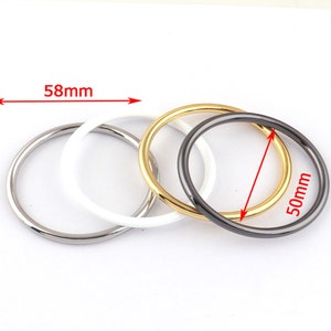 May include: Four metal rings in silver, white, gold, and dark gray. The rings are approximately 2 inches in diameter and 2.3 inches in width. The rings are arranged in a slightly overlapping pattern, showcasing their different colors and finishes.